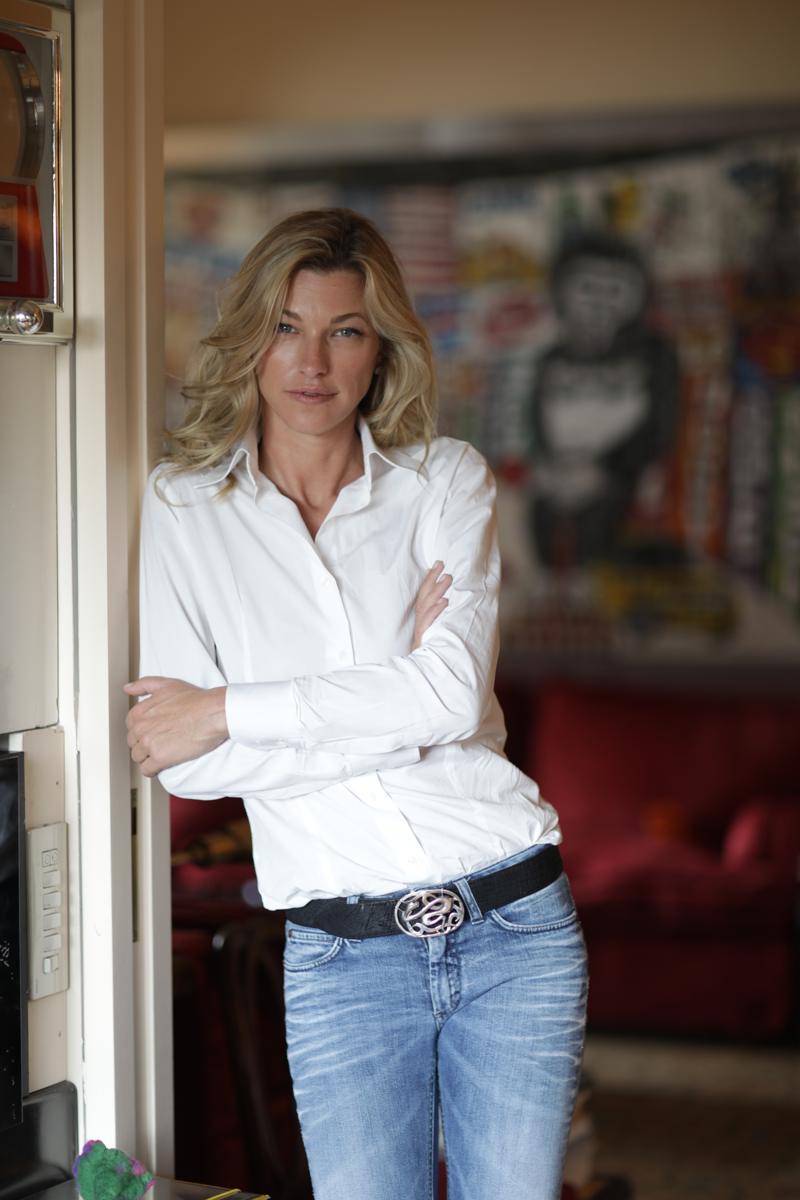 Nicole Junkermann in a white shirt leaning in a doorway at home with framed artwork behind her