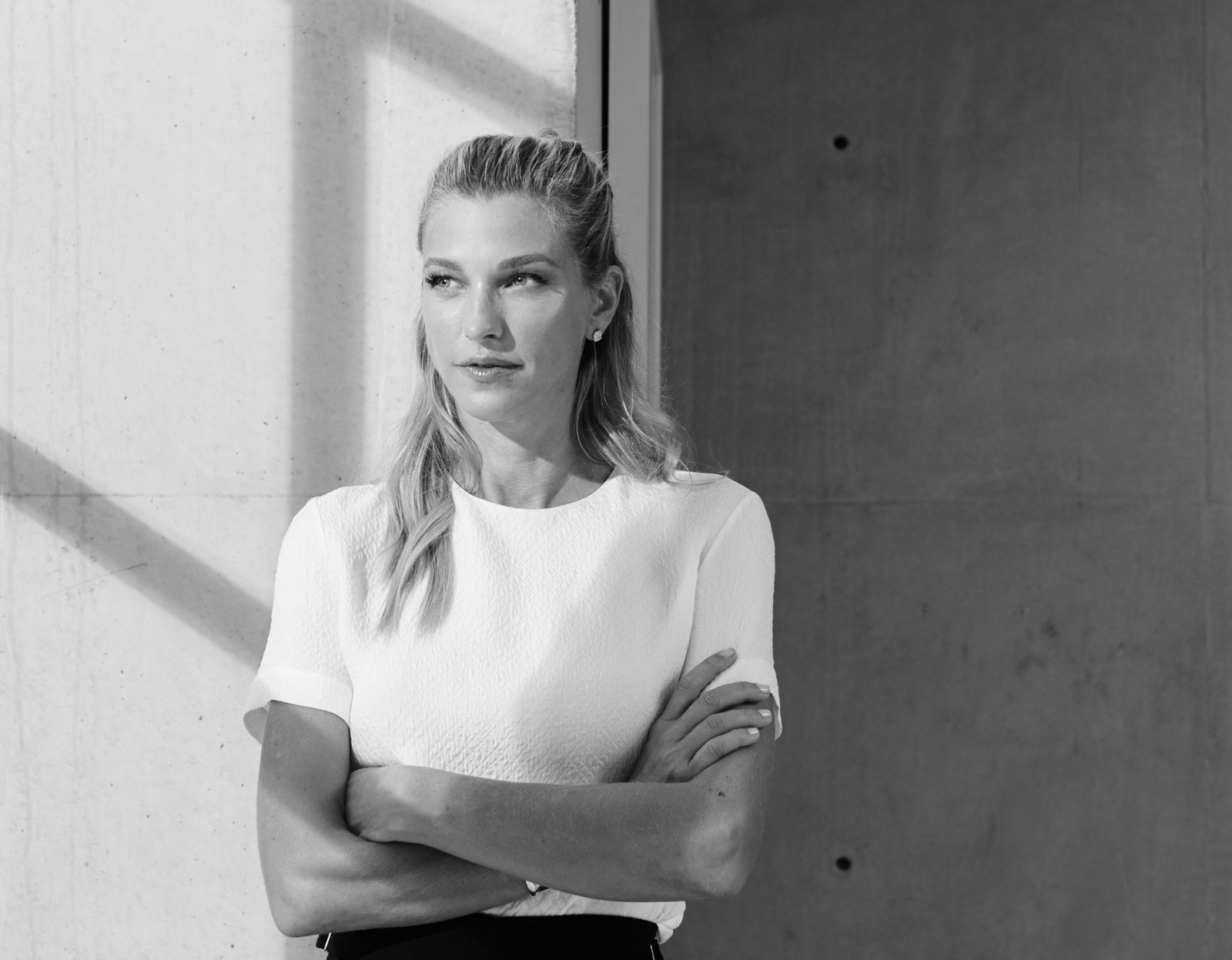Nicole Junkermann in a white top, standing against a sunlit concrete wall in a calm editorial portrait