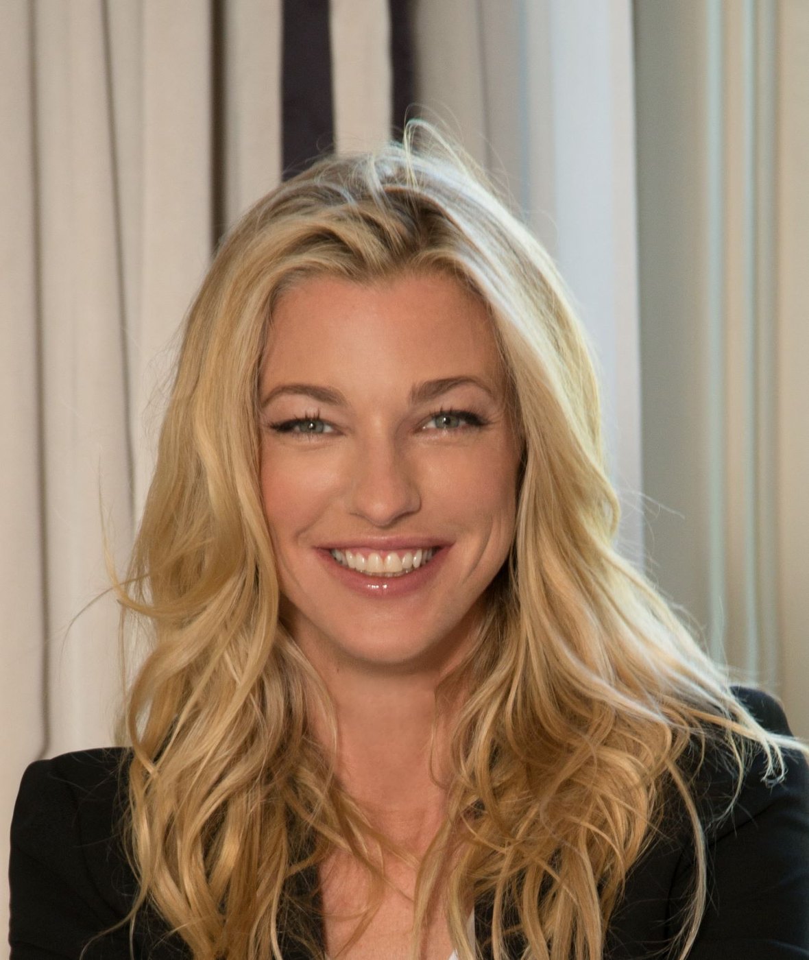 Portrait of Nicole Junkermann with blond hair, smiling warmly at the camera in a bright room